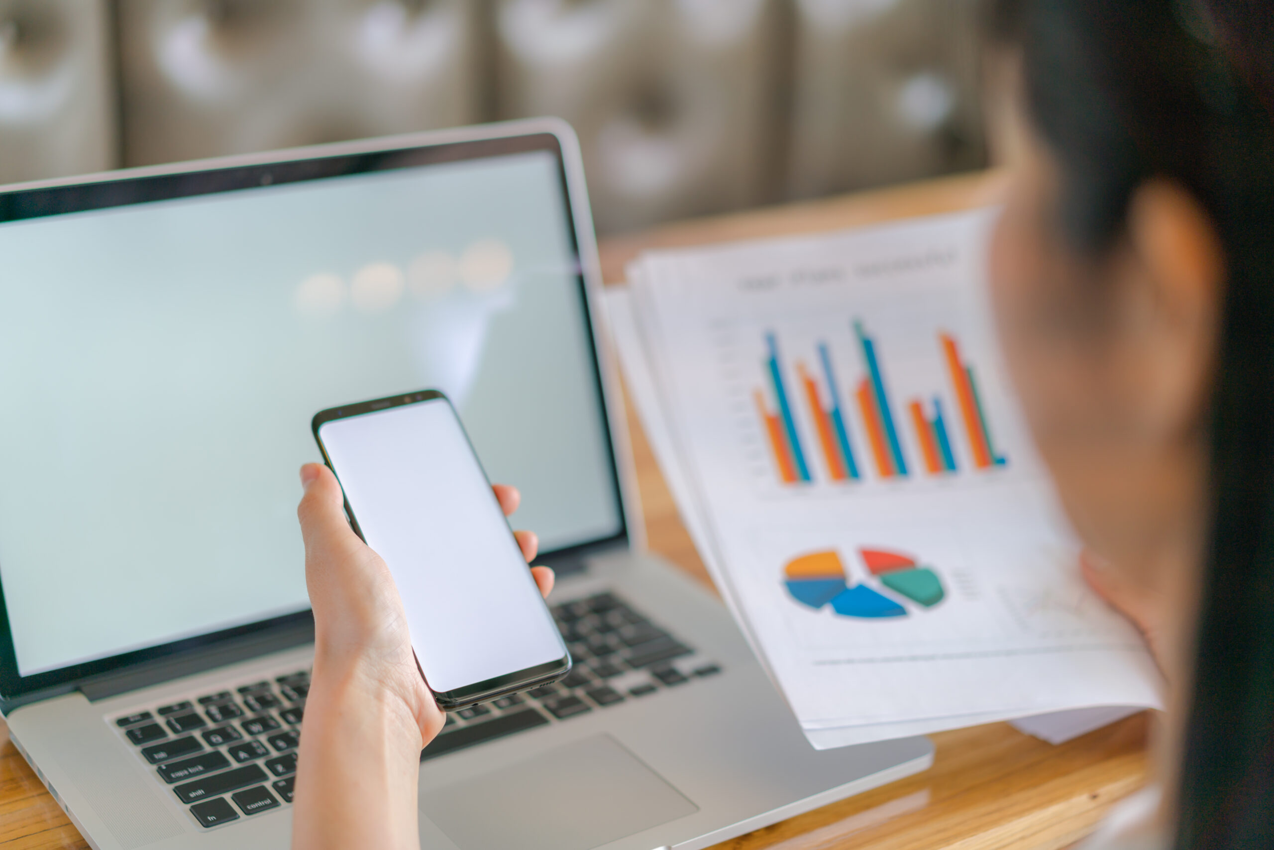 Business woman hand with Financial charts and mobile phone over laptop on the table